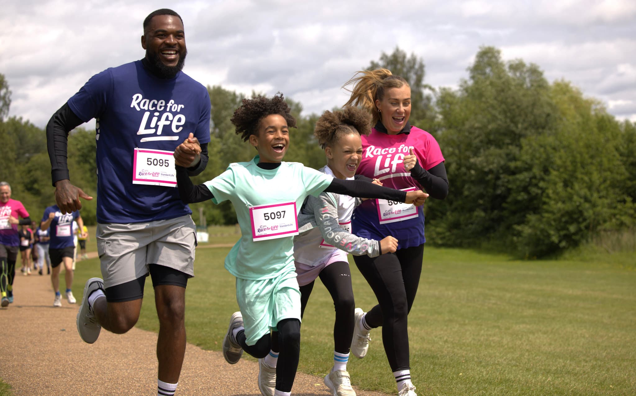 Two adults and two children wearing Race for Life T-shirts running with smiles on their faces.