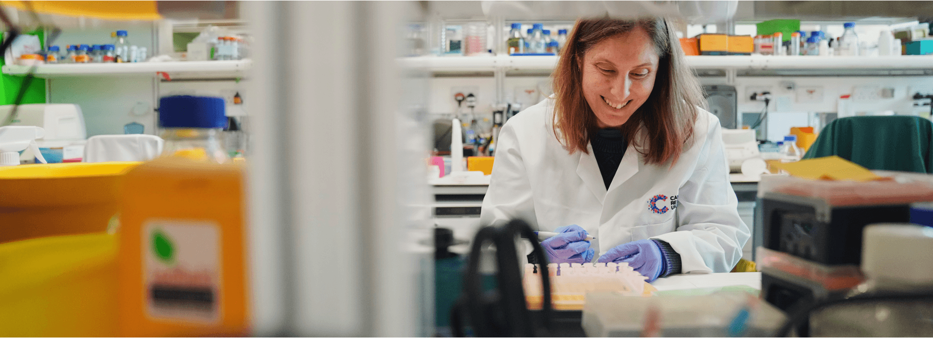 A scientist in a white lab coat working with a smile on her face.