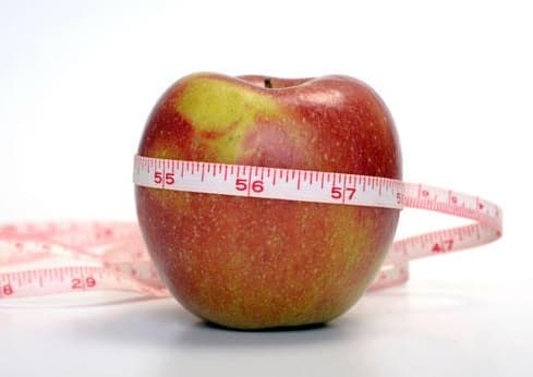 An apple with a tape measure wrapped around it.