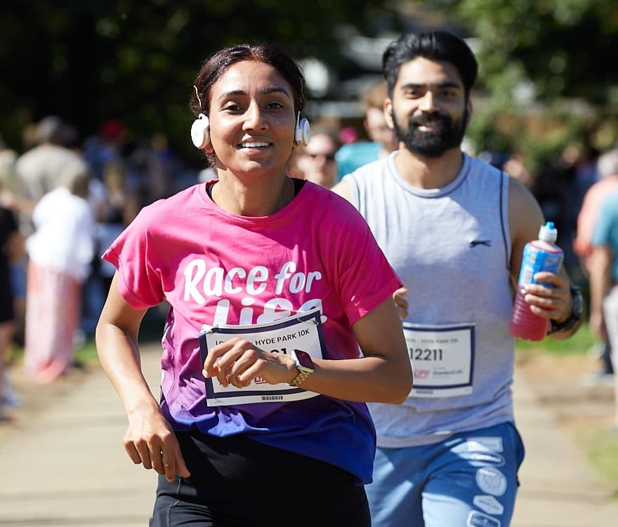 Image of 2 race for life 10k runners. One is wearing and pink and purple ombre race for life tshirt and headphones.