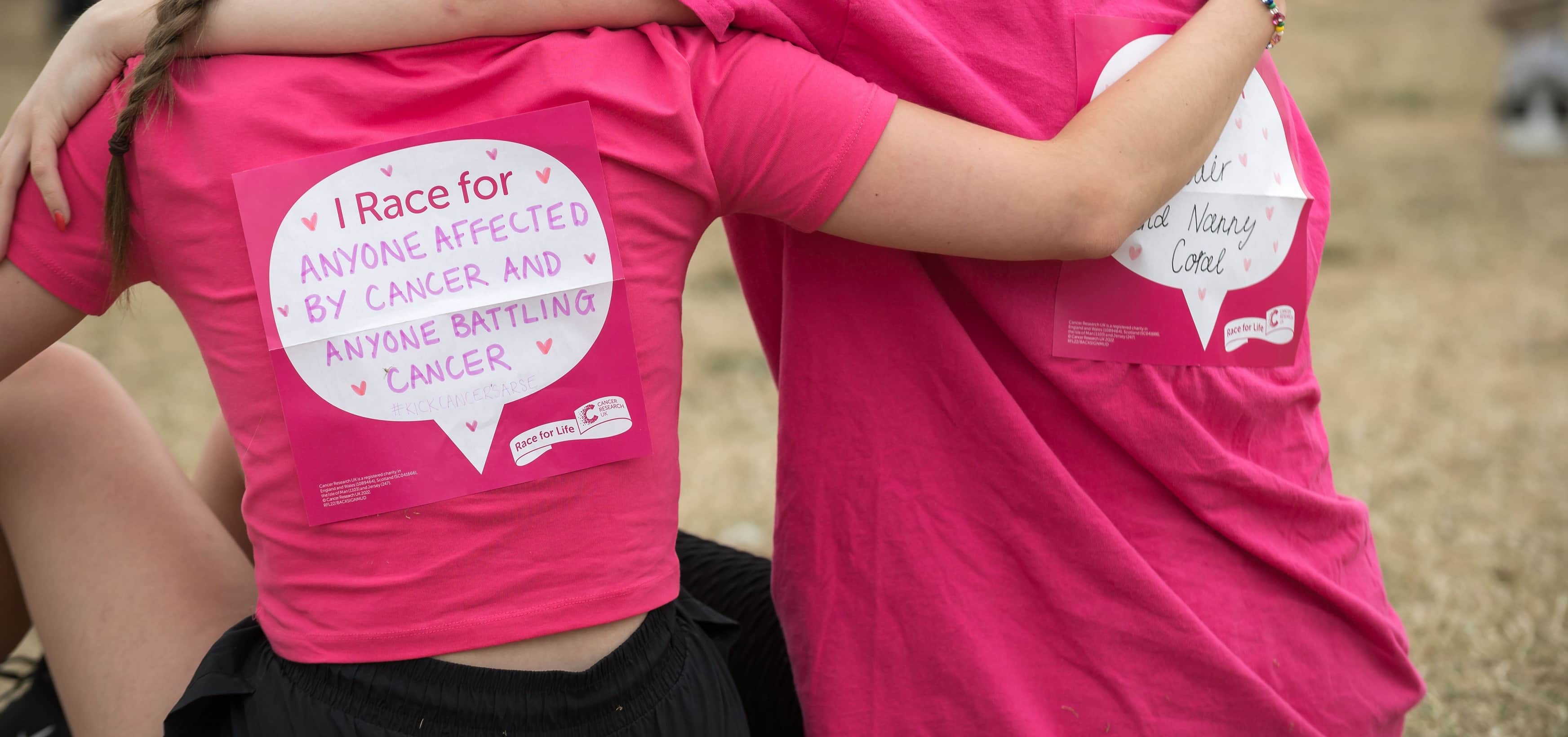 Two people hugging. The back sign reads 'I race for anyone affected by cancer and anyone battling cancer'.